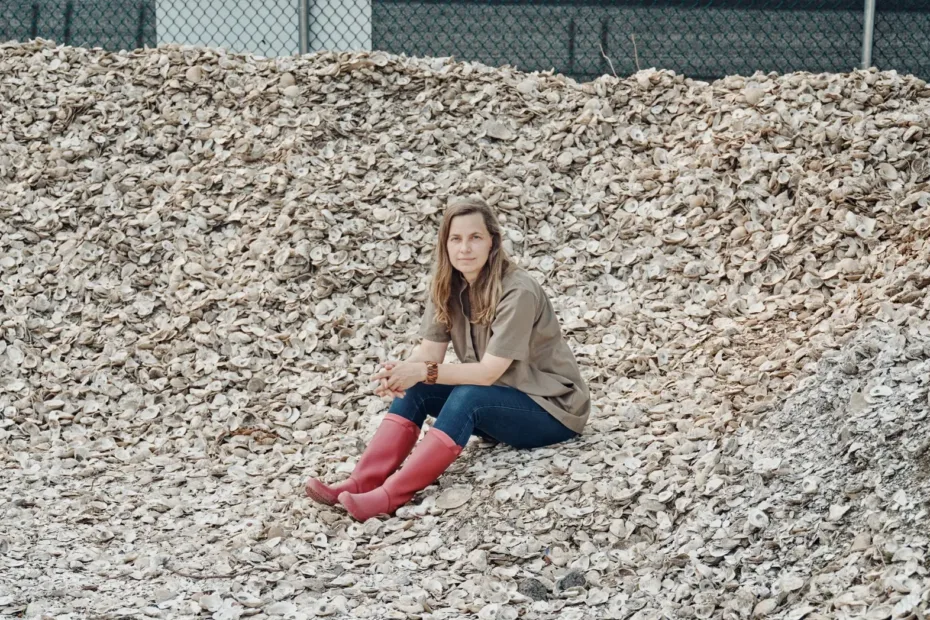 Frau sitzt auf großer Menge Austernschalen, vor ihr zwei Körbe mit Austern