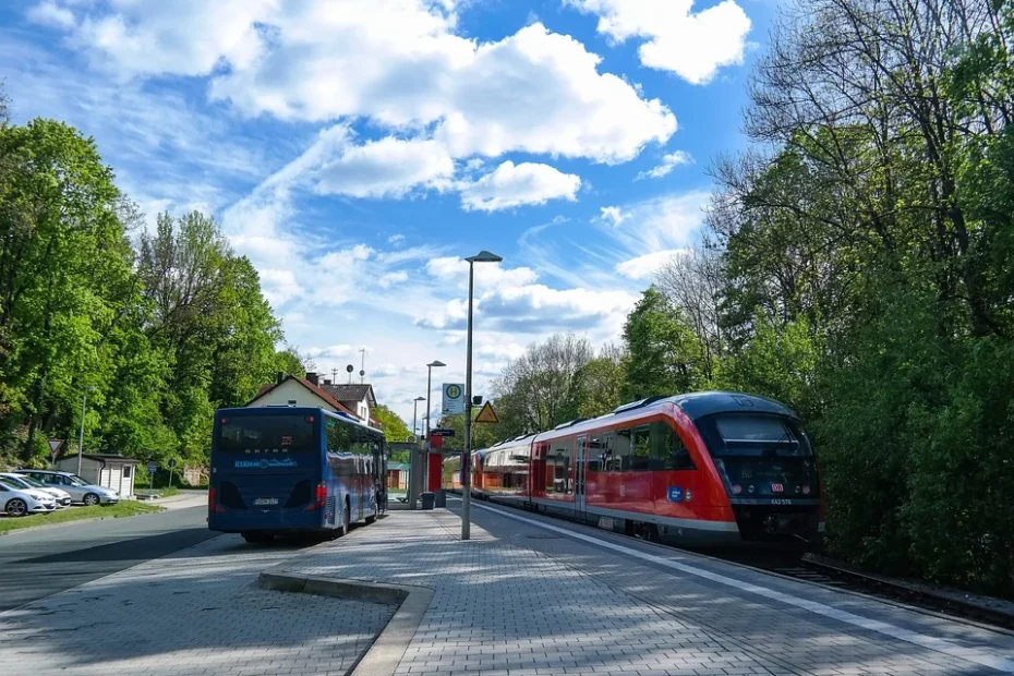 An einem Bahnhof stehen Bus und Bahn vor blauem Himmel mit Wolken