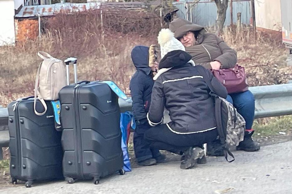 Drei Personen mit Gepäck warten an der Grenze darauf zu erfahren, ob und wie es weitergeht