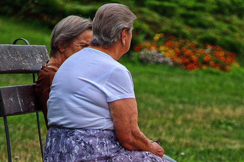 zwei alte Damen sitzen im Grünen auf einer Bank und unterhalten sich