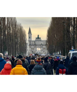 Photographie der Demonstration gegen Rechts am 21. Januar 2024 in München, zu sehen Bäume, Menschen von hinten, ein Tor/Triumphbogen und ein Turm